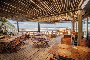 Une terrasse extérieure en bois, dotée de tables et de chaises, qui offre une vue sur l’océan.