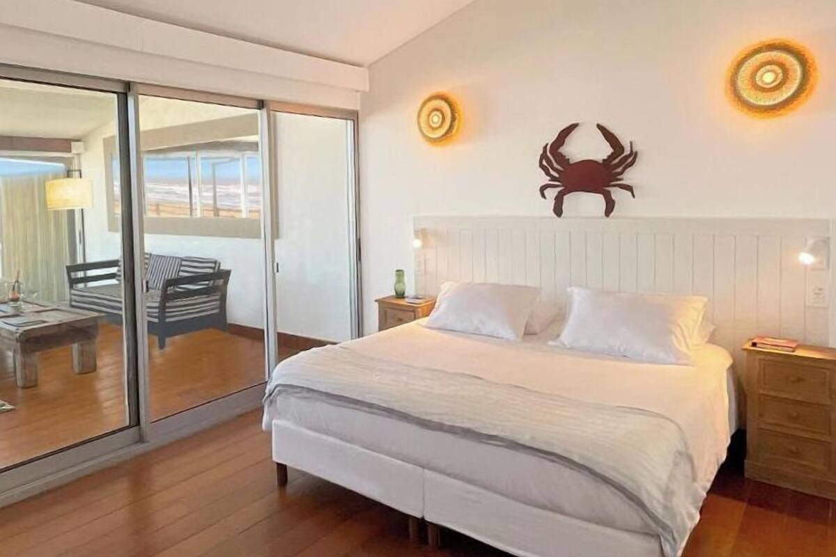 A bedroom with a large bed, a sliding glass door leading to a balcony, and a wall-mounted crab decoration.