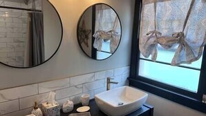 Une salle de bain avec deux miroirs ronds, un lavabo blanc et une fenêtre ornée de rideaux à motifs.
