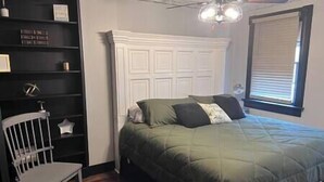 Une chambre à coucher avec un lit, une chaise, une armoire blanche et une fenêtre avec des stores.