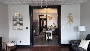 Un salon doté d’un parquet en bois foncé, d’un canapé en cuir noir, d’un tapis blanc et d’un coin repas avec une table et des chaises.