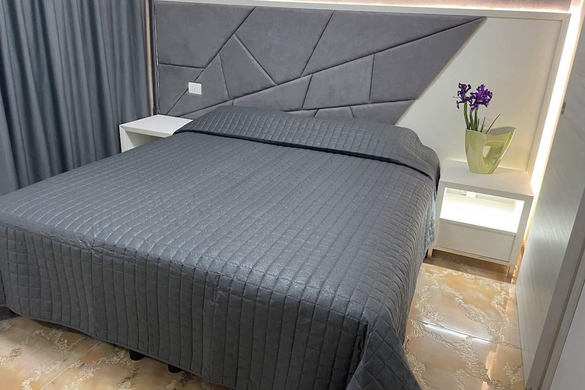 Een moderne slaapkamer met een bed, nachtkastjes en een vaas met bloemen.