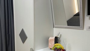 Une petite pièce moderne, avec un bureau blanc, une chaise, un miroir et un saladier rempli de fruits.