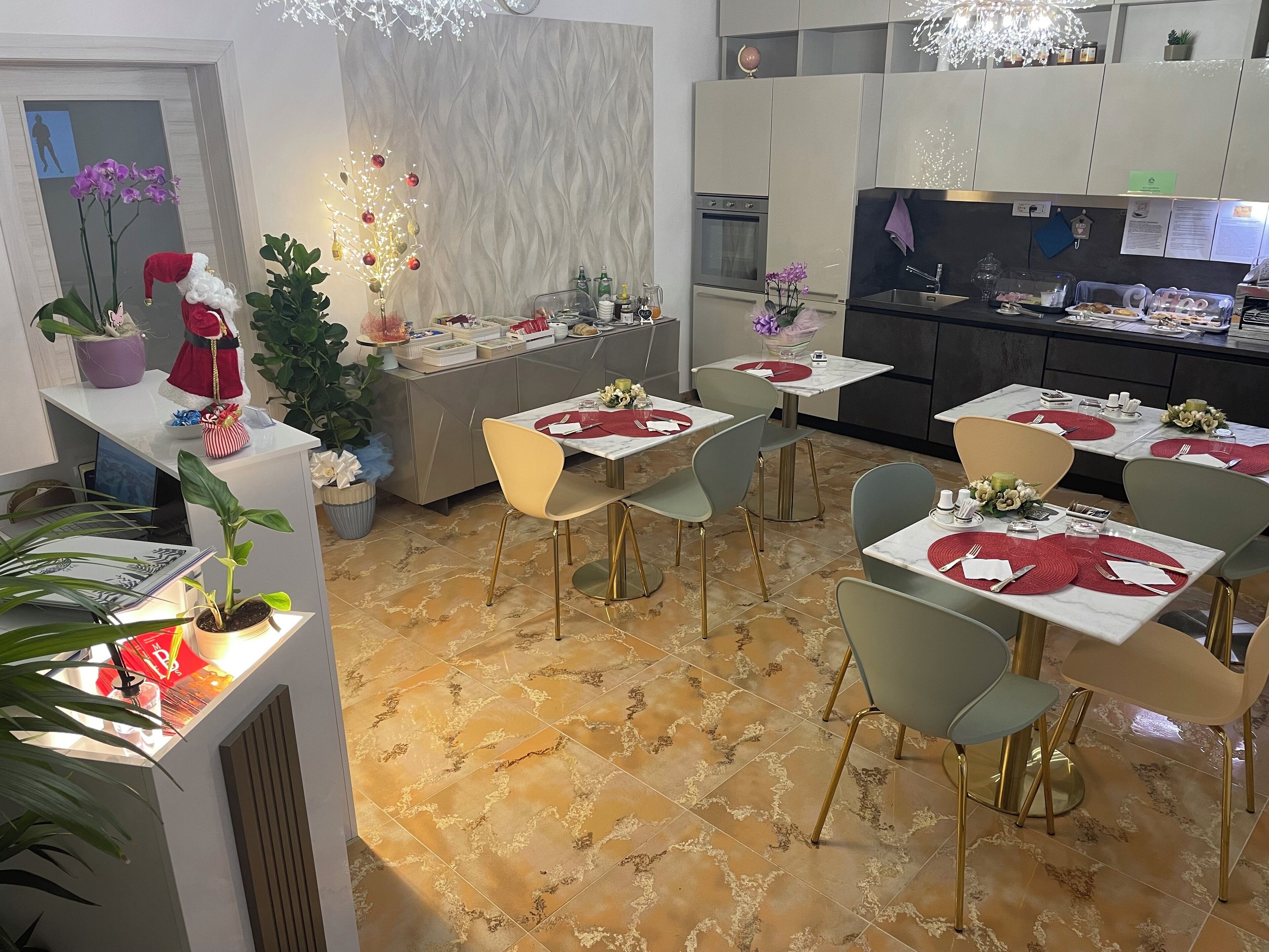 A modern dining area with multiple tables and chairs, a kitchen in the background, and decorative plants and ornaments.