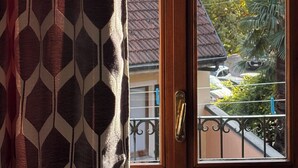 A view through a wooden door with a geometric patterned curtain, leading to a balcony with a metal railing, a mountain, and trees in the background. - Oh!megna in the historic heart (Omegna)