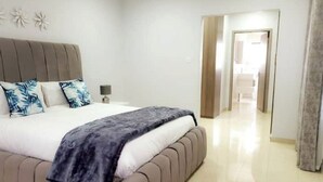 Ein Schlafzimmer mit einem großen Bett, einem Nachttisch und einer Tür zu einem anderen Raum.