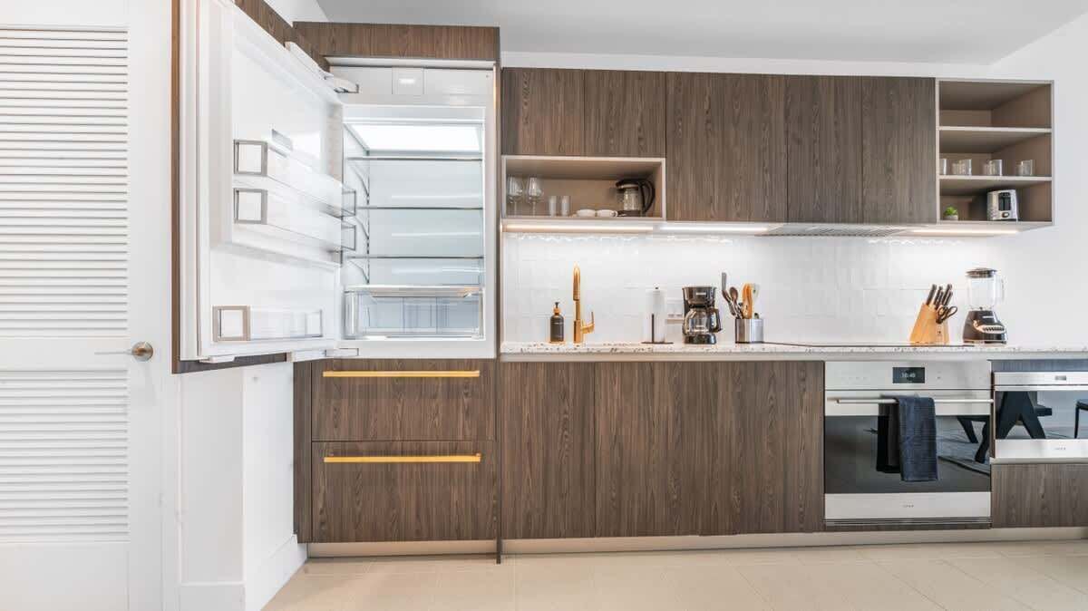 Una cocina moderna con armarios de madera, horno empotrado y encimera con diversos electrodomésticos y utensilios.