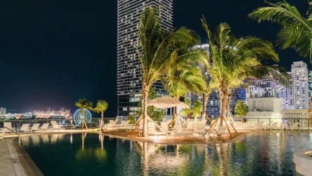 A nighttime pool area with palm trees, a Ferris wheel, and high-rise buildings in the background. - Lux 2BR Condo With Pool, Spa & Gym Access (Miami)