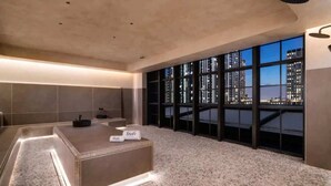 A modern hotel room with a large window offering a city view, a well-lit reception desk, and a spacious layout. - Lux 2BR Condo With Pool, Spa & Gym Access (Miami)