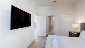 A hotel room with a bed, a TV mounted on the wall, a bedside table with a lamp, and a door leading to a bathroom. - 5BR Villa w/ Pvt Pool, 15 Min to Disney, Sleeps 10 (Davenport)