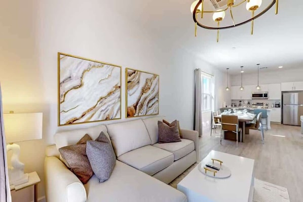 A modern living room with a sofa, a dining table, and a kitchen in the background.