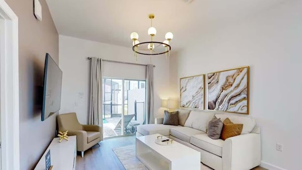 A modern living room with a white sofa, a coffee table, and a chandelier. - 5BR Villa w/ Pvt Pool, 15 Min to Disney, Sleeps 10 (Davenport)