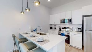 A modern kitchen with white cabinetry, stainless steel appliances, and a central island with seating. - 5BR Villa w/ Pvt Pool, 15 Min to Disney, Sleeps 10 (Davenport)