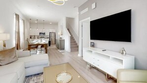 A modern living room with a flat-screen TV, white furniture, and a staircase leading to a kitchen. - Modern 5BR Villa w/ Pool Near Disney (Davenport)