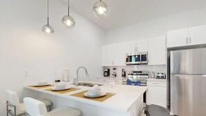 A modern kitchen with white cabinetry, a stainless steel refrigerator, and a central island with bar stools. - Modern 5BR Villa w/ Pool Near Disney (Davenport)