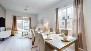 A modern dining area with a long table set for a meal, a sofa, and a TV in the background. - Modern 5BR Villa w/ Pool Near Disney (Davenport)