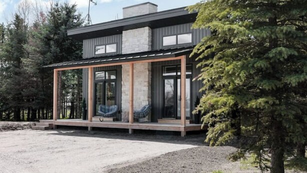 Una casa moderna con amplios ventanales de vidrio, una chimenea de piedra y una terraza de madera.