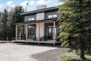 Et moderne hus med store glasvinduer, en stenskorsten og en træterrasse.