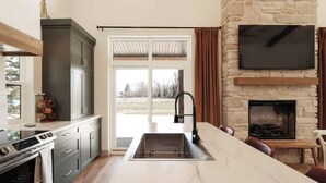 Una cocina moderna con chimenea de piedra, un televisor grande montado encima y una zona de comedor con una isla de mármol.