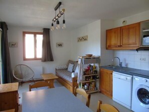 Uma cozinha compacta com armários de madeira, máquina de lavar embutida e um espaço de refeições com mesa e cadeiras.