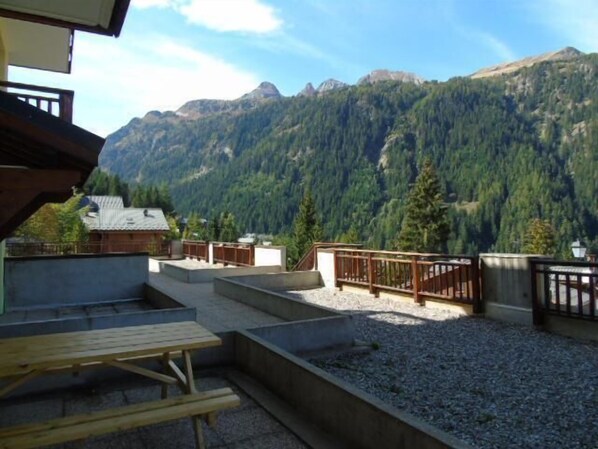 A terrace with a wooden table and benches, overlooking a mountainous landscape.