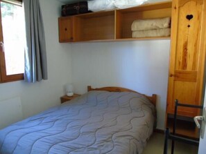 Quarto com cama, mesa de cabeceira, guarda-roupa e janela com cortinas.