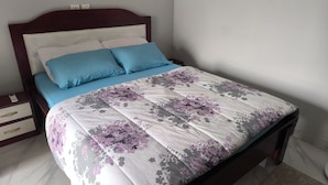 A neatly made bed with a floral bedspread, a wooden headboard, and a nightstand with drawers. - SOTIDEK YOP (Abidjan)