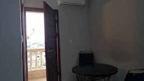 A room with a balcony door, an air conditioning unit, a table, and a chair. - SOTIDEK YOP (Abidjan)