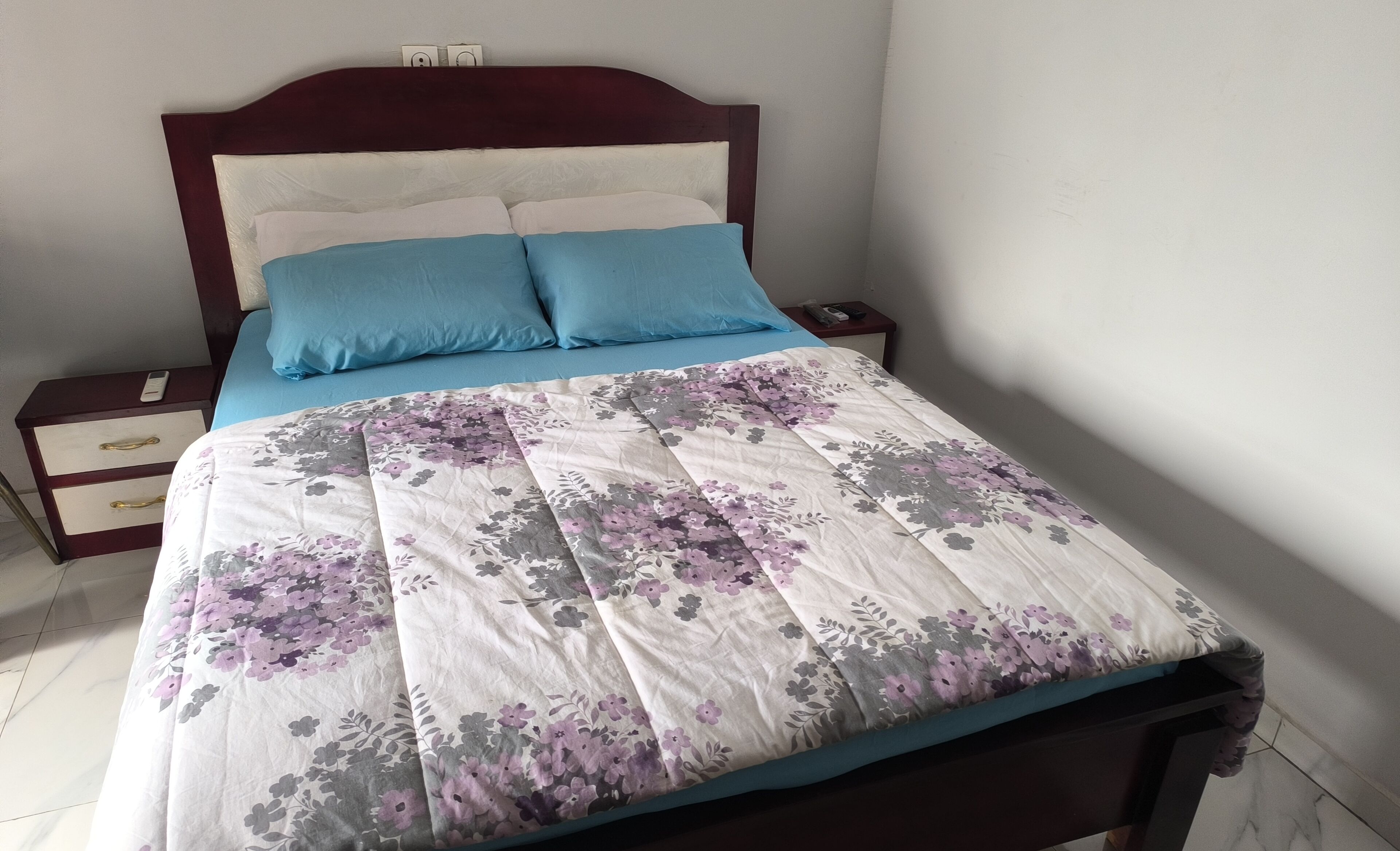A bed with a floral bedspread, a wooden headboard, and a bedside table with a phone.