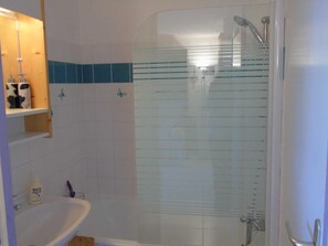 Ein Badezimmer mit einer Duschkabine, einem weißen Waschbecken und einer Holzeinrichtung für Toilettenartikel.