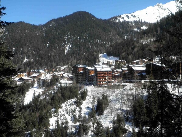 Un chalet de montagne composé de plusieurs bâtiments, entouré de pentes enneigées et de forêts denses.
