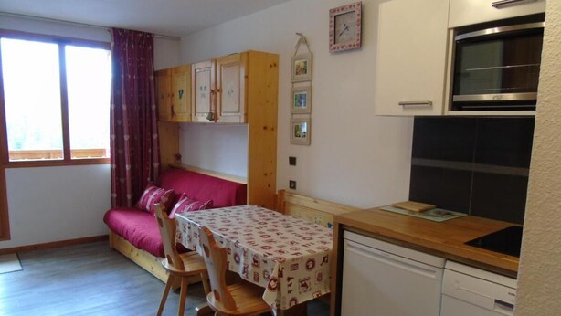 A compact kitchen with a dining table, chairs, a sofa, and a dishwasher.