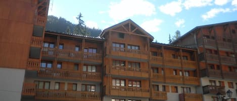 A multi-story hotel with wooden balconies and a ski resort backdrop.
