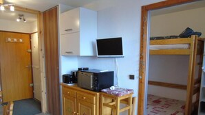 A compact room with a wooden desk, a bunk bed, a television, and a small kitchenette.