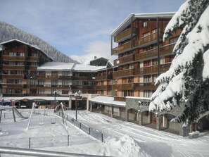 Um hotel com vários andares, varandas, uma pista de esqui e uma montanha nevada ao fundo.