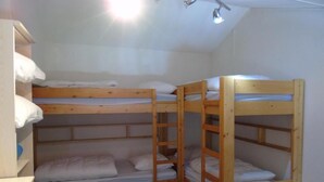A bunk bed room with a wooden bunk bed, a shelf with folded clothes, and a desk.