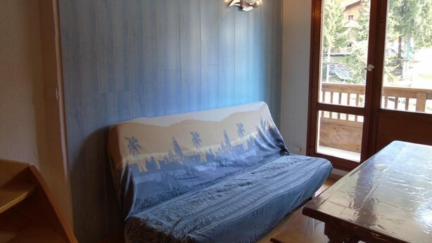A room with a bed, a wooden table, and a door leading outside.