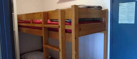 A dormitory room with bunk beds, a ladder, a shelf, and a door with a notice.