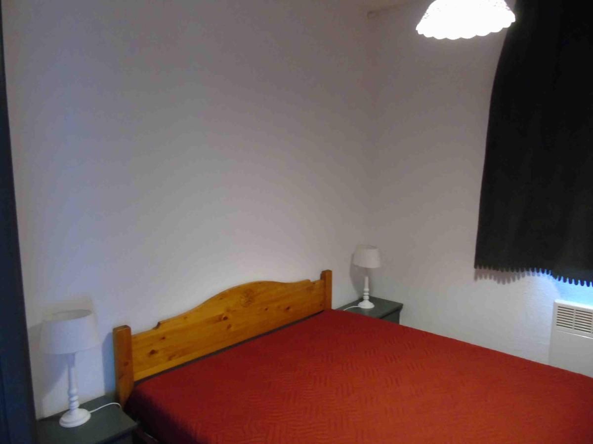 Una habitación pequeña y sencilla con una cama de madera, una mesita de noche con lámpara y un calentador fijado a la pared.
