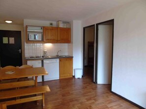 A compact kitchen with wooden cabinets, a microwave, and a dishwasher. There is a dining table with benches and a trash bin. - 5th floor, view resort, balcony, tv, ski locker, 36m², Valfréjus (Valfréjus)