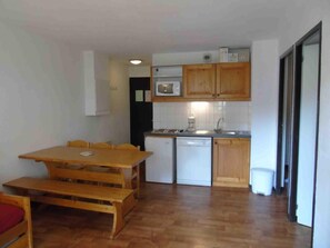 A compact kitchen with wooden cabinets, a microwave, a sink, and a dishwasher. There is a wooden dining table with benches.