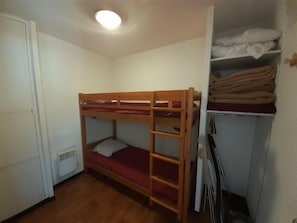 A bunk bed with a red mattress, a white door, and a white wardrobe with folded clothes.