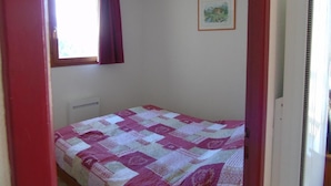 A small, sparsely furnished room with a single bed, a window with curtains, a radiator, and a framed picture on the wall. - 5th floor, view mountain, balcony, tv, ski locker, 34m², Valfréjus (Valfréjus)