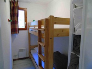 A small, narrow room with a bunk bed, a window with curtains, and a radiator.
