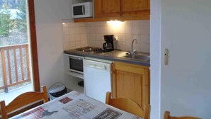 Cozinha compacta com armários de madeira, micro-ondas, máquina de café e lava-louças.