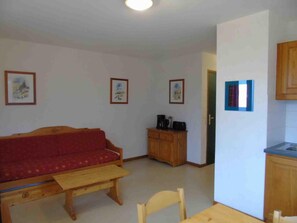 A compact living space with a sofa, a wooden table, a cabinet, and a kitchenette area.