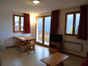 A room with a wooden dining table and chairs, a TV on a wooden stand, and large windows with curtains. - 2nd floor, view valley, balcony, tv, ski locker, 36m², Valfréjus (Valfréjus)
