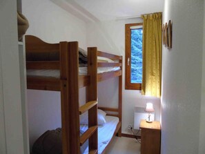 Ein Schlafraum mit Etagenbetten, einem Fenster, einem Nachttisch mit Lampe und einer Heizung.