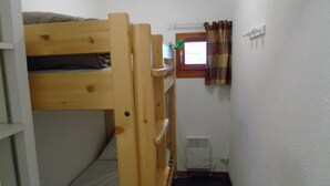 A bunk bed room with a window, a radiator, and a curtain.