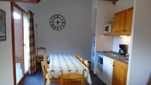 A dining area with a table set for six, a clock on the wall, and a kitchen with wooden cabinets and a microwave.
